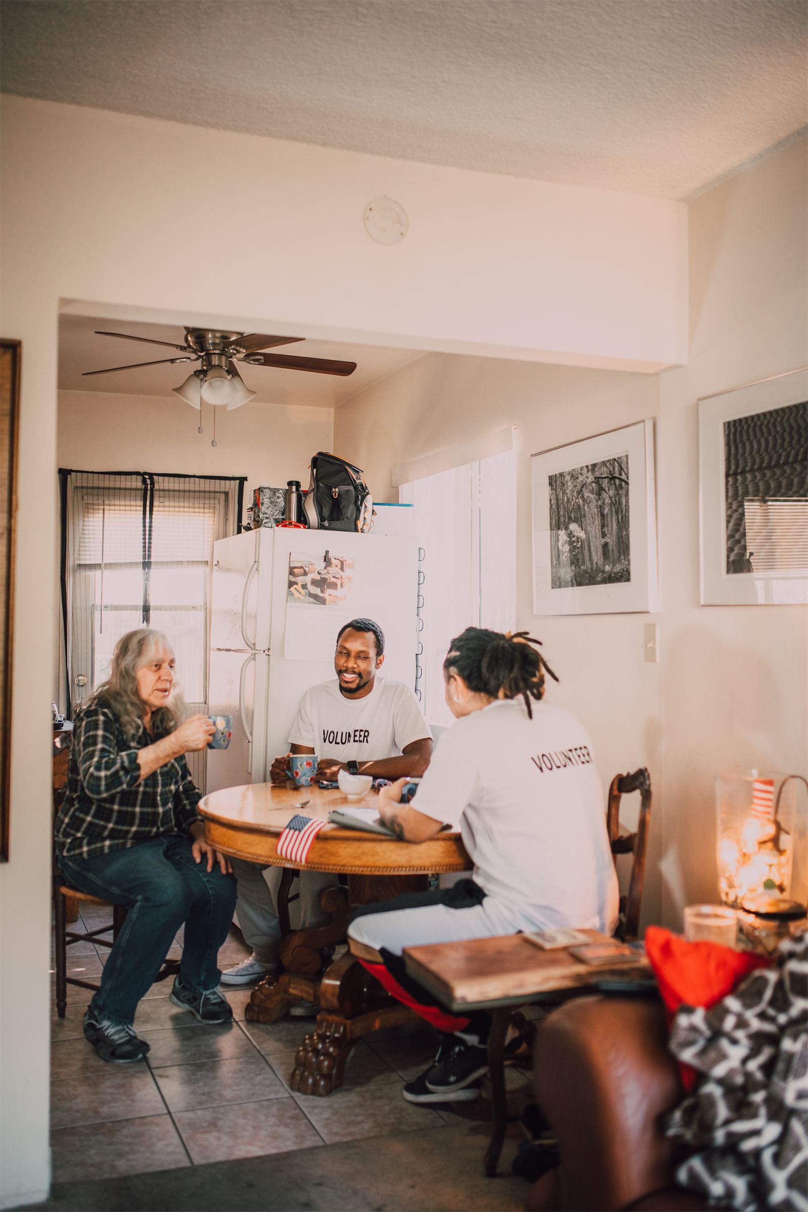 Volunteers sharing a warm moment with a resident at her kitchen table.